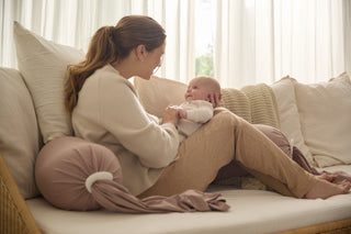 Woman sitting on a couch holding a baby in a cozy living room.