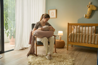 A mom feeding her baby with a pregnancy pillow in a nice nursery setting.