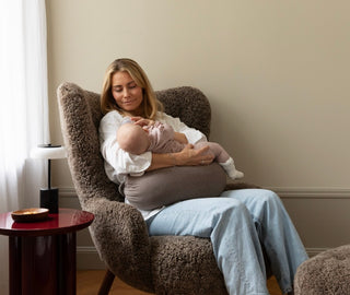 A woman bottle-feeding her baby with a brown Nursing Pillow