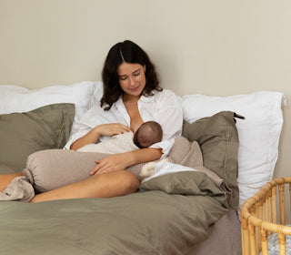 A woman breastfeeding her baby in bed with a Nursing Pillow